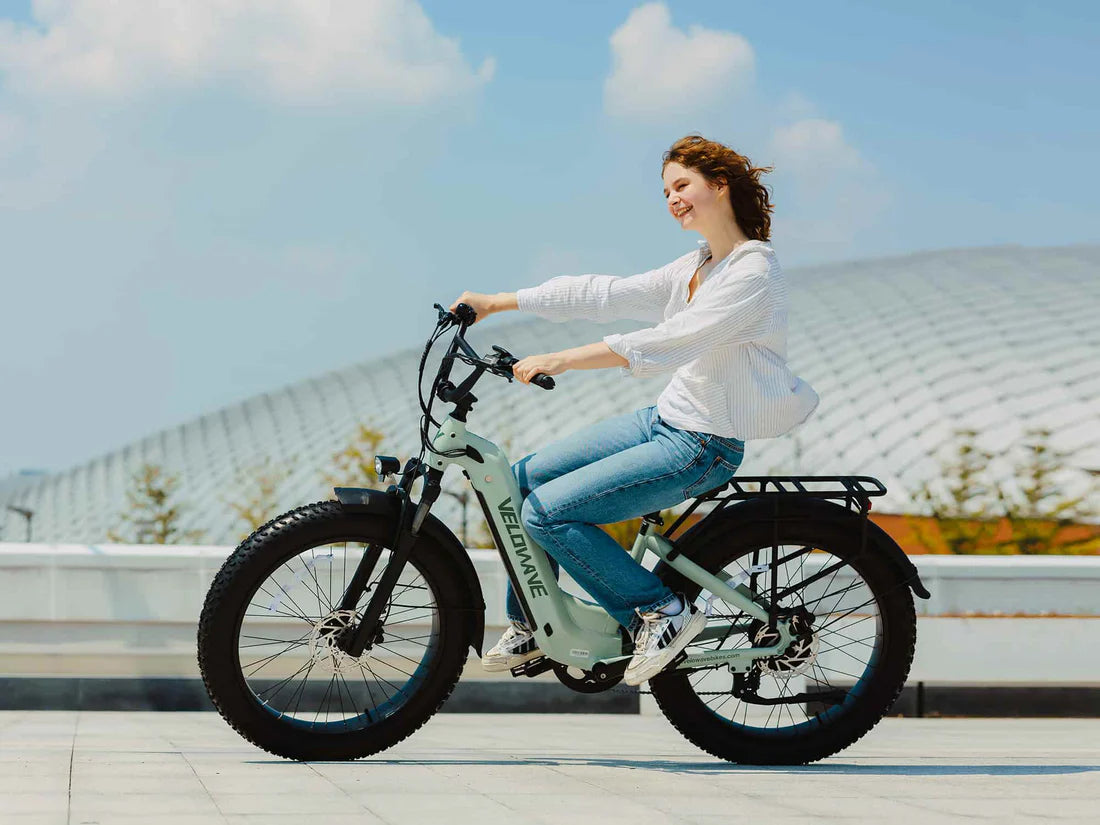 Velowave Ranger Step-Thru 3.0 Torque Sensor Electric Bike Woman riding a light blue electric bike with a modern building in the background. Valowave Ranger Step-Thru 3.0 Torque Sensor Electric Bike