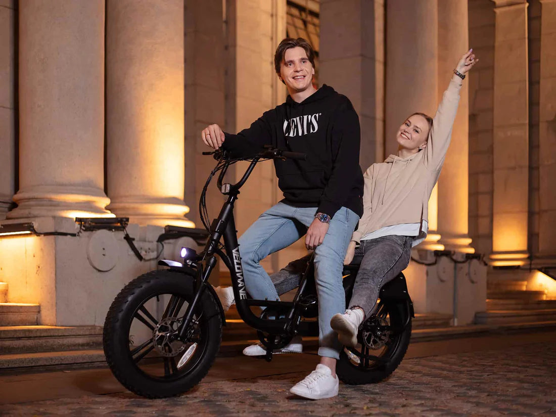 Velowave Prado S Commuter Electric Bike Two people on a black electric bike in front of classical architecture. Valowave Prado S Commuter Electric Bike