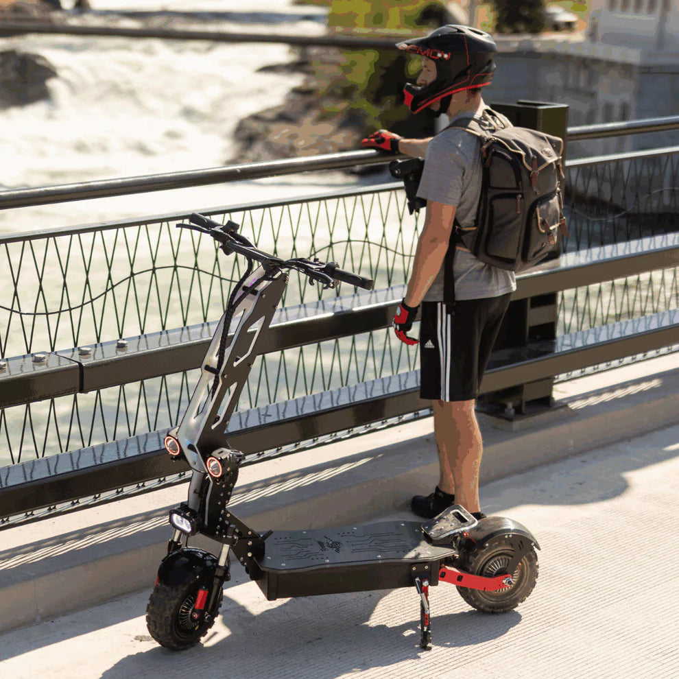 Freego D11 Landtiger Electric Scooter Foldable Dual Motor 4000W Person with a backpack standing next to a folded electric scooter on a bridge. Freego D11 Landtiger Electric Scooter Foldable Dual Motor 4000W