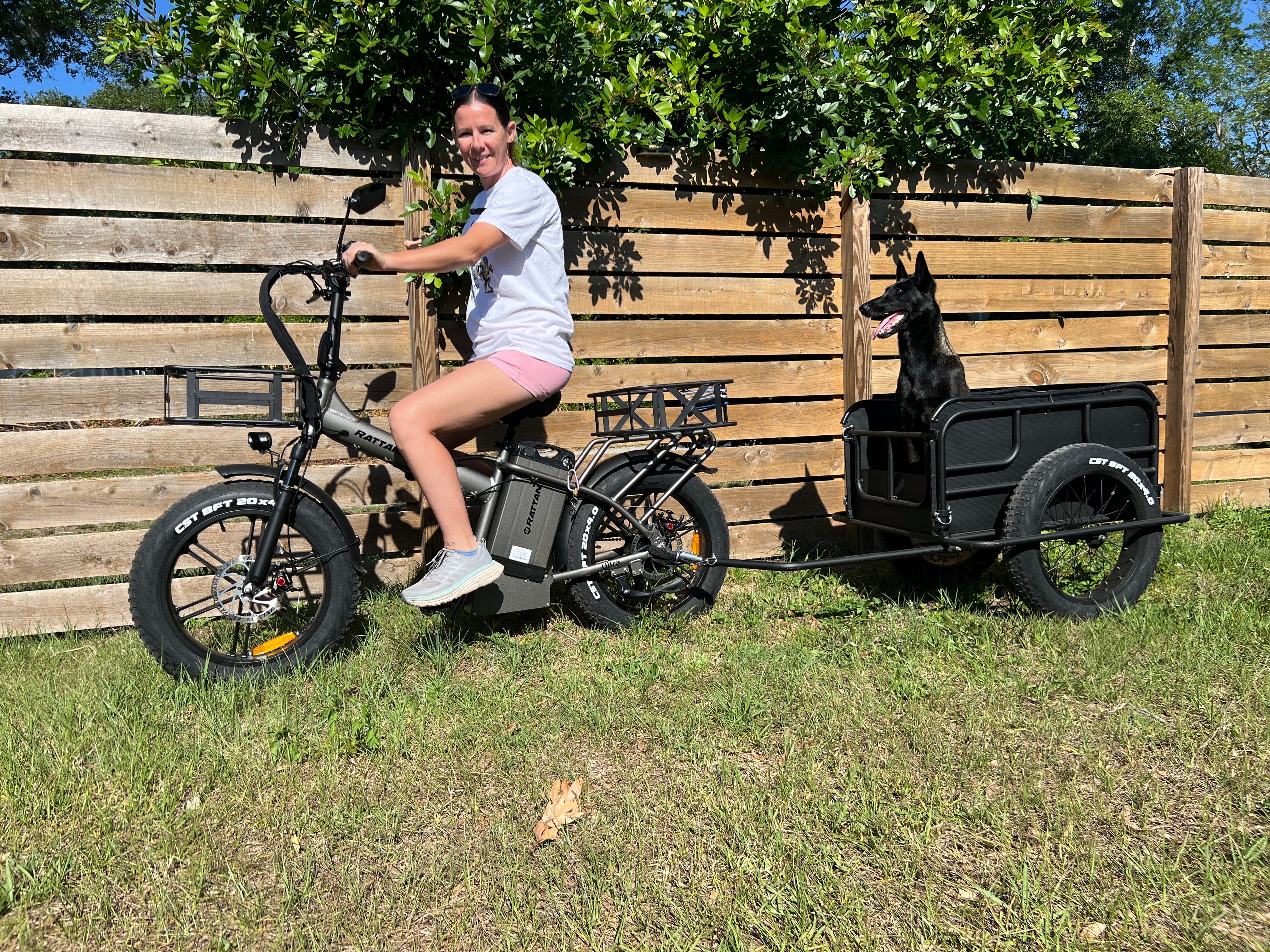 Rattan LM Ultra Folding ebike Person riding a bike with a trailer attached, featuring a dog inside, against a wooden fence background. Rattan LM Ultra Folding ebike