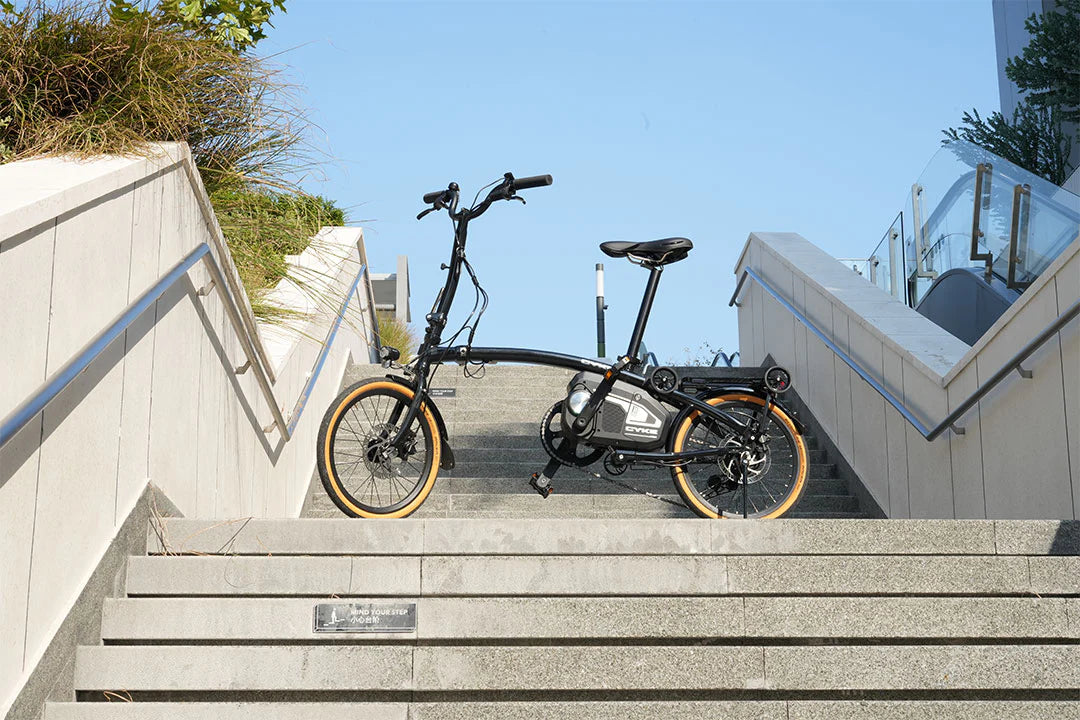 CYKE Kingfisher Mid-Drive Folding eBike Foldable bicycle on a set of stairs with a clear blue sky in the background. CYKE Kingfisher Mid-Drive Folding eBike