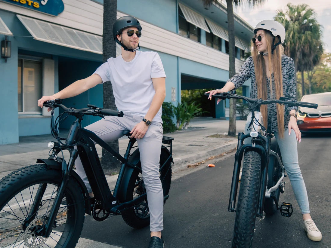 Velowave Ranger 2.0 Fat Tire All-Terrain Electric Bike Two people on electric bikes in an urban setting with a building and car in the background. Valowave Ranger 2.0 Fat Tire All-Terrain Electric Bike
