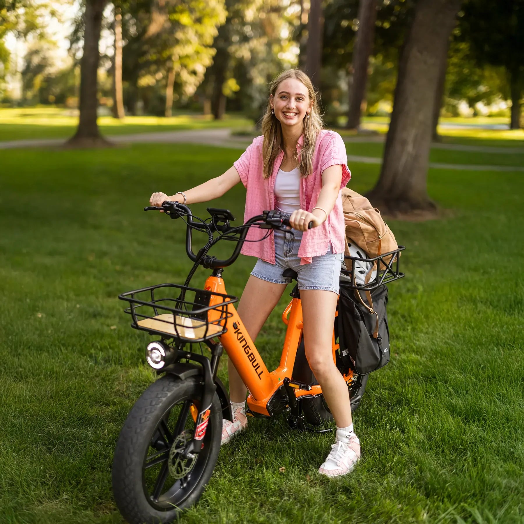 Kingbull Voyager 2.0 Fat Tire Electric Cargo Bike Woman standing with an orange electric bike in a park. Kingbull Voyager 2.0 Fat Tire Electric Cargo Bike
