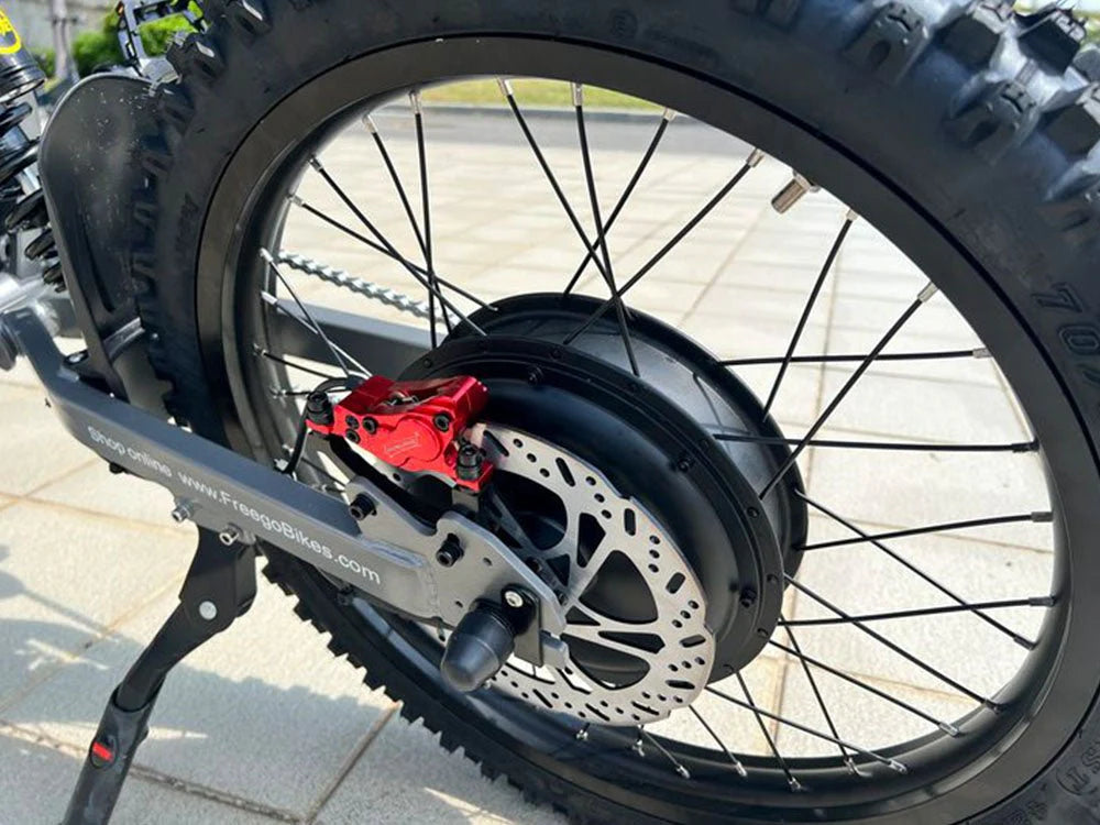 Freego X2 Pro All-Terrain Dirt eBike Close-up of a bicycle wheel with a red component on a paved road. Freego X2 Pro All-Terrain Dirt eBike