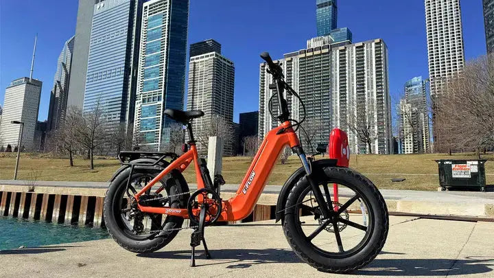 YOUNG Electric E-Flow 750W Folding eBike Orange electric bike parked on a sidewalk with city skyline in the background. YOUNG Electric E-Flow 750W Folding eBike