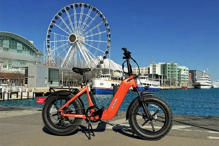 YOUNG Electric E-Flow 750W Folding eBike Orange electric bike parked on a dock with a Ferris wheel and waterfront in the background. YOUNG Electric E-Flow 750W Folding eBike