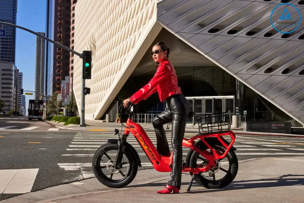 CYKE COLLIE Cargo EBike Person riding a red electric bike on a city street with modern architecture. COLLIE Cargo EBike