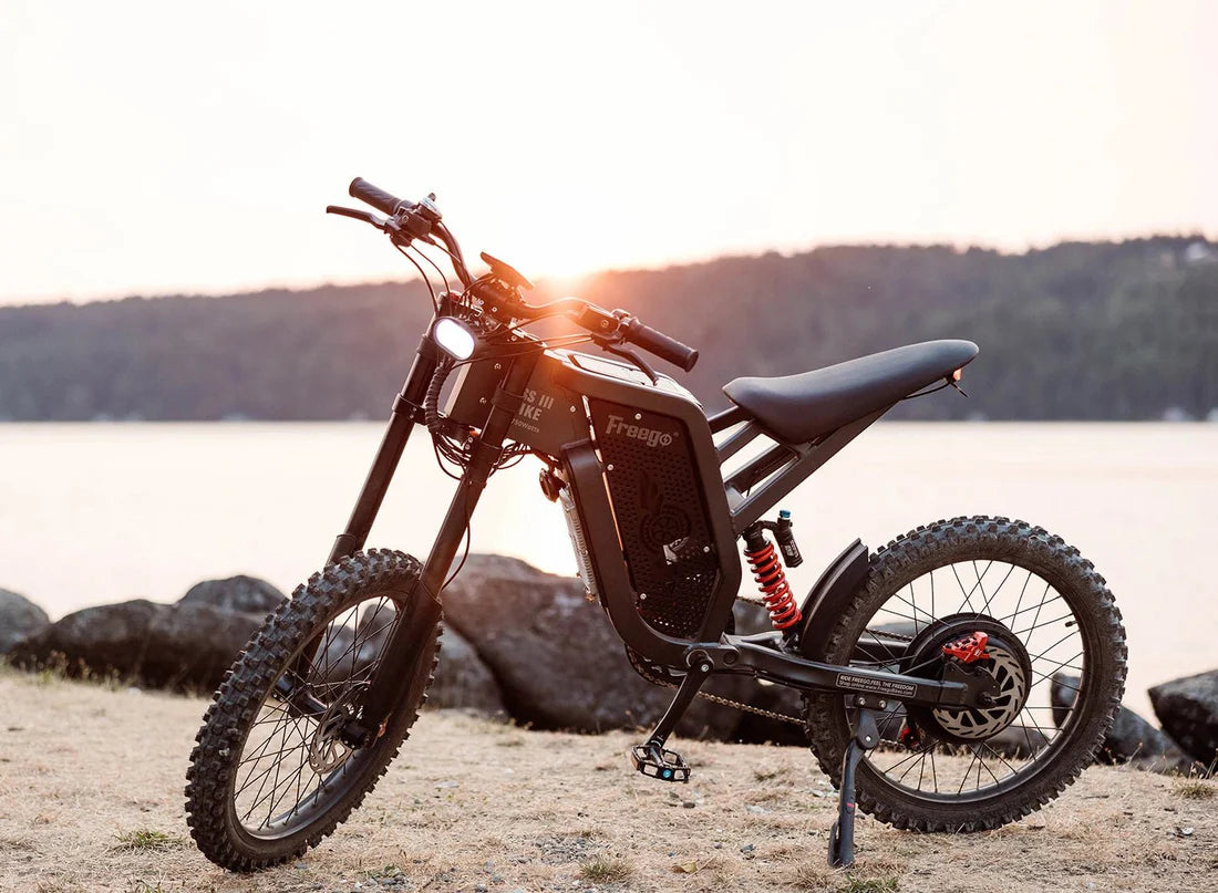 Freego X2 Dirt Master Off-Road eBike Motorcycle parked on a rocky shore with a sunset in the background. Freego X2 Pro All-Terrain Dirt eBike