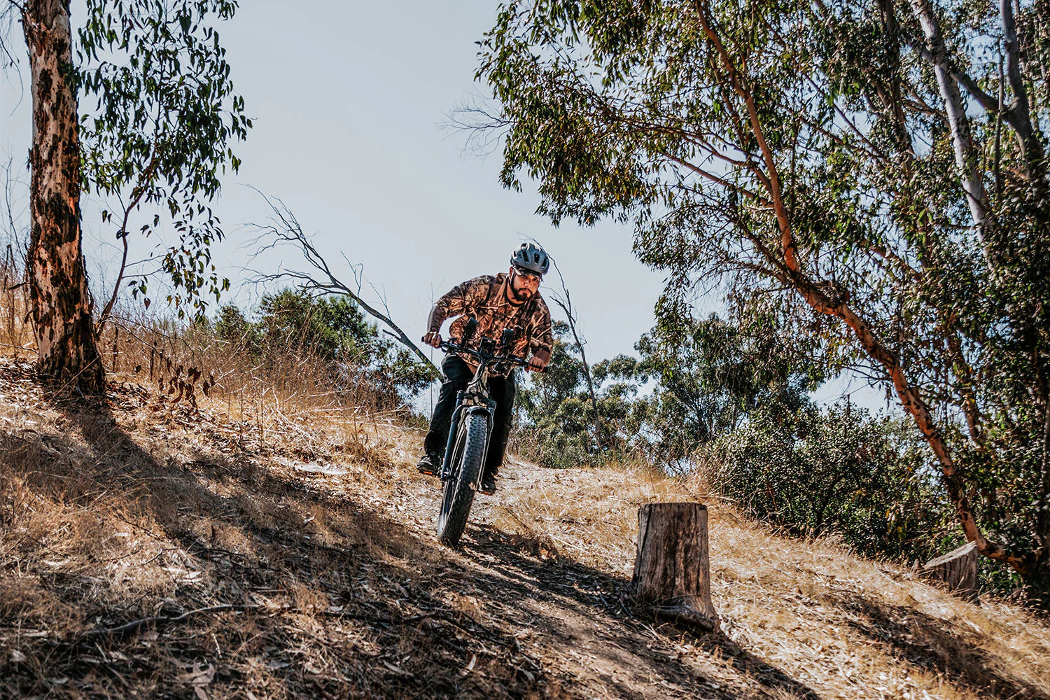 CYKE Cheetah Hunting EBike Person riding a mountain bike on a trail with trees and a clear sky. CYKE Cheetah Hunting EBike