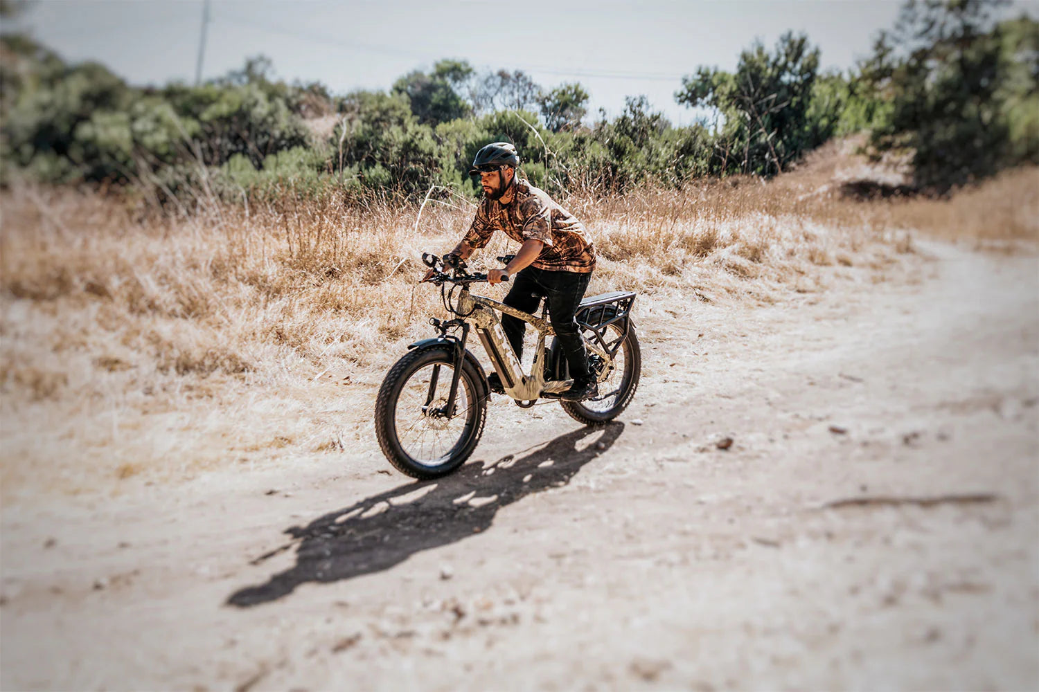 CYKE Cheetah Hunting EBike Person riding a bike on a dirt path with dry grass and trees in the background. CYKE Cheetah Hunting EBike