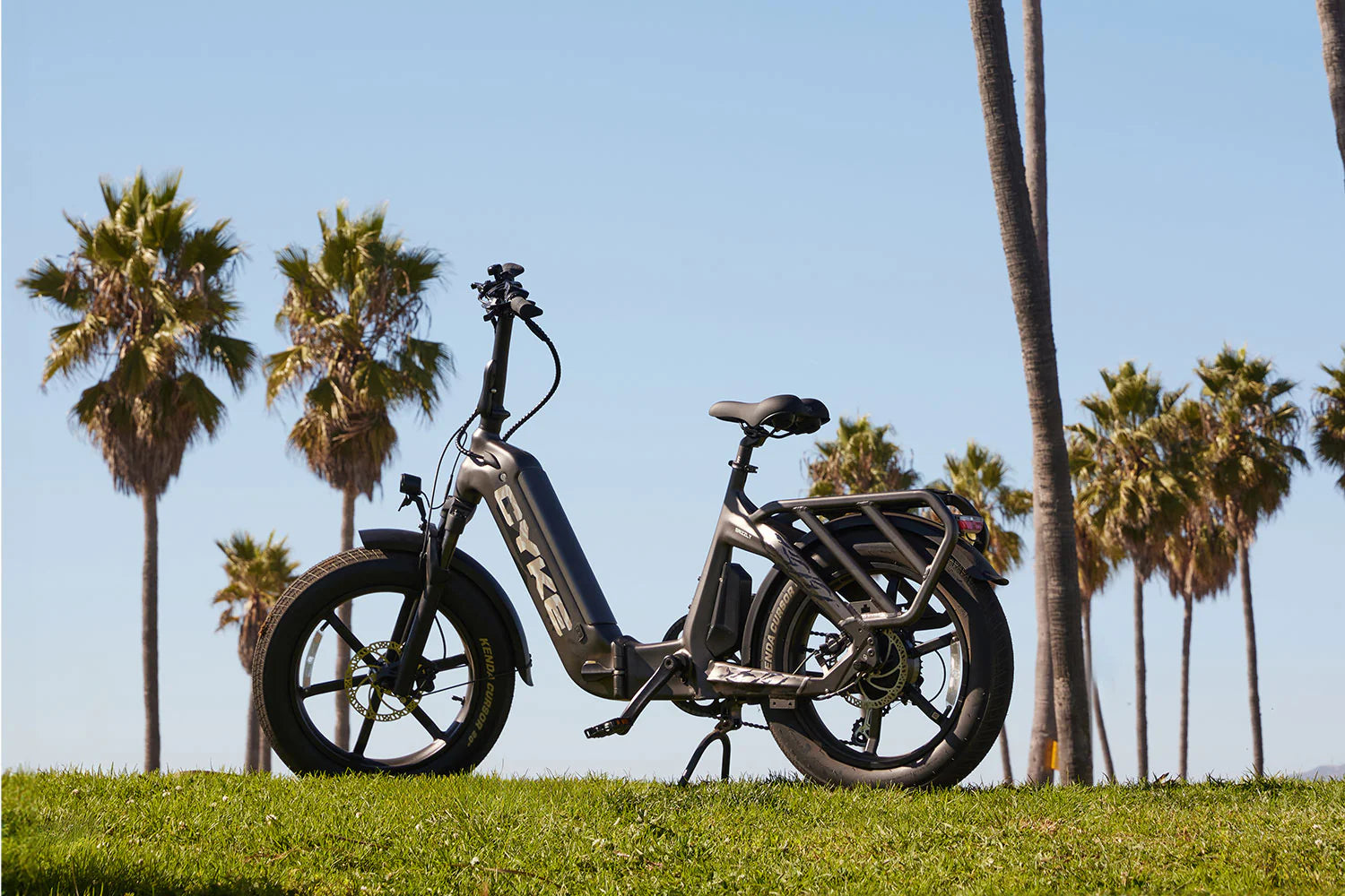 CYKE Grizzly Foldable EBike Electric bike on grass with palm trees in the background. CYKE Grizzly Foldable EBike
