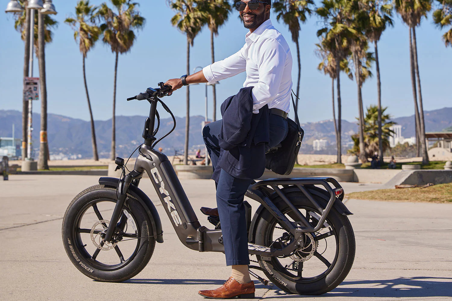 CYKE Grizzly Foldable EBike Man sitting on an electric bike with palm trees and a beach in the background. CYKE Grizzly Foldable EBike