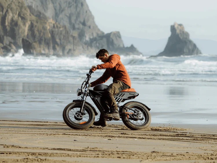 Freego Flash F3 Pro Max Dual Motor and Battery eBike Person riding a beach bike on a sandy beach with ocean waves and rocky cliffs in the background. Freego Flash F3 Pro Max Dual Motor and Battery eBike