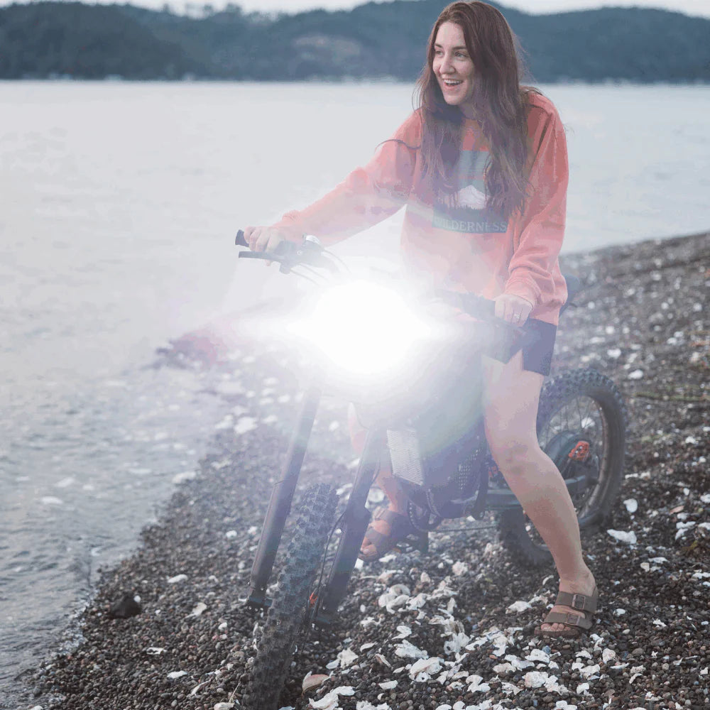 Freego X2 Dirt Master Off-Road eBike Woman with a bicycle on a pebbly beach near water. Freego X2 Pro All-Terrain Dirt eBike