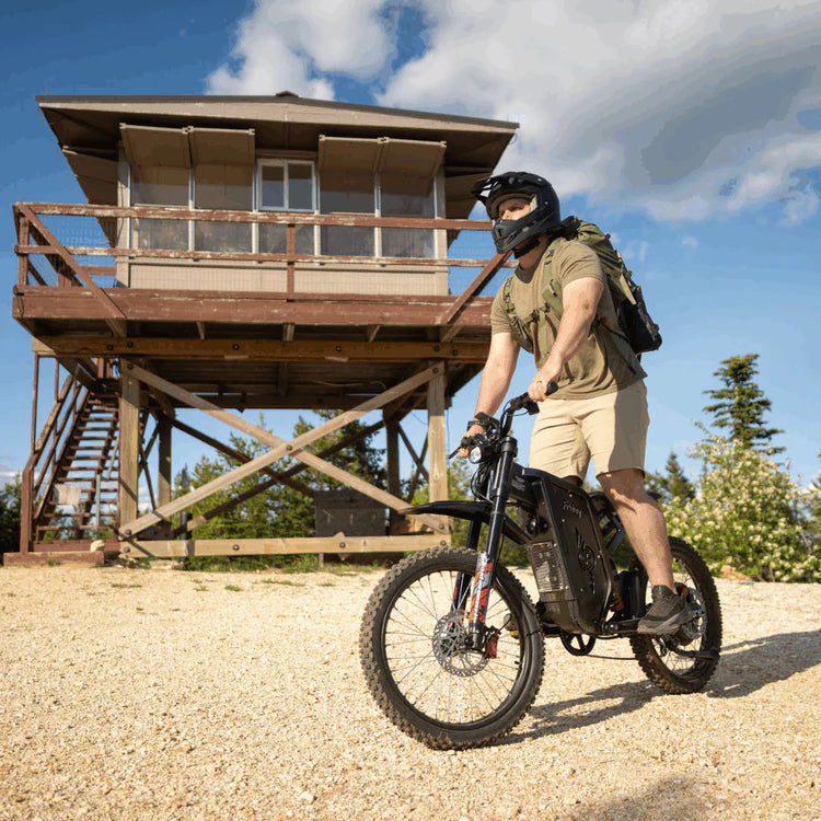 Freego X2 Pro All-Terrain Dirt eBike Person riding a motorized bike near a wooden lookout tower on a sunny day. Freego X2 Pro All-Terrain Dirt eBike