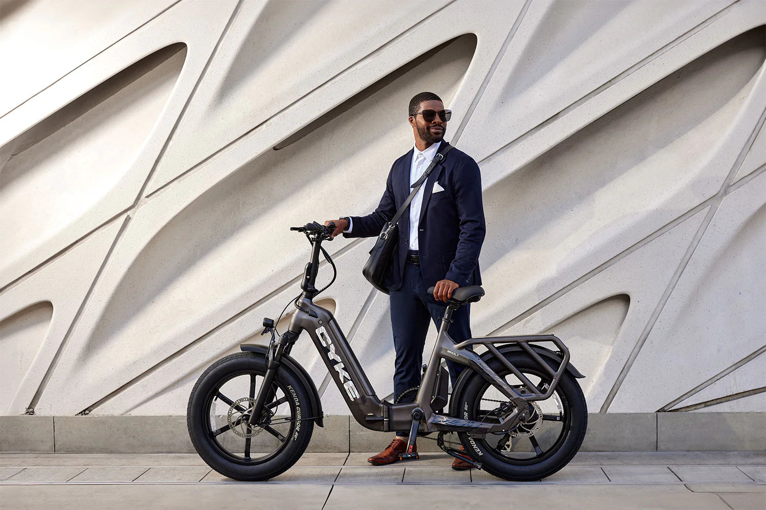 CYKE Grizzly Foldable EBike Man in a suit standing next to an electric bike against a modern architectural background. CYKE Grizzly Foldable EBike
