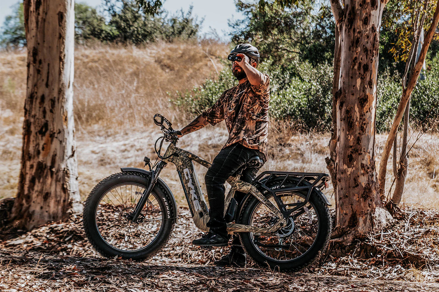 CYKE Cheetah Hunting EBike Man sitting on a fat-tire bike in a natural setting with trees and dry grass. CYKE Cheetah Hunting EBike
