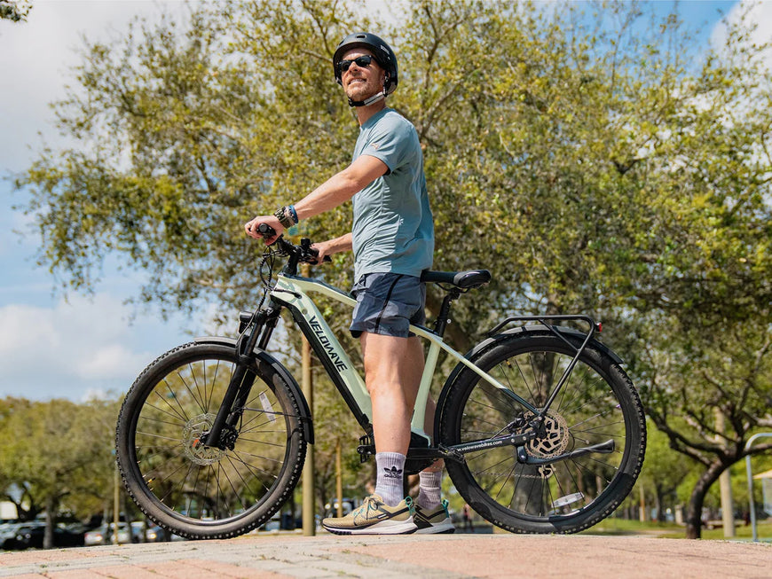 Man standing next to a bicycle on a path with trees in the background. Valowave Swift M Mid-Drive Electric Bike