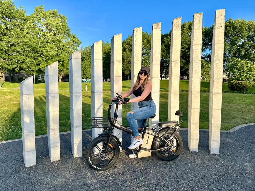 Person riding a bike in a park with stone pillars and greenery. Rattan LM Ultra Folding ebike