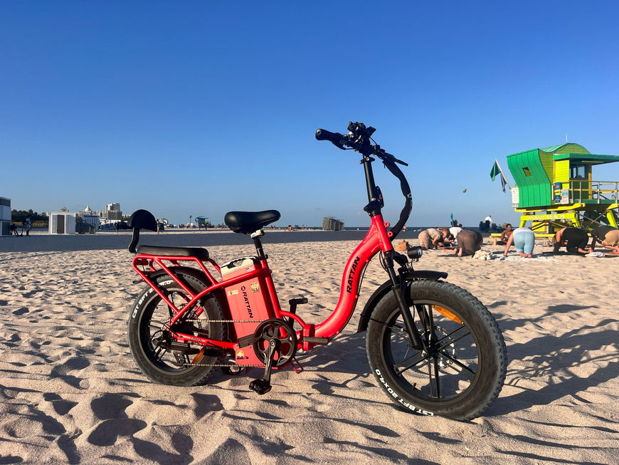 Red electric bike on a sandy beach with a lifeguard tower in the background. Rattan LF Ultra Folding ebike
