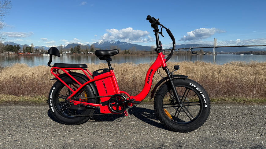Red electric bike on a paved path with a scenic background of water and mountains. Rattan LF Ultra Folding ebike