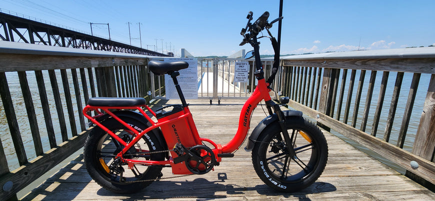 Red electric bike on a wooden pier with water and sky in the background. Rattan LF Ultra Folding ebike