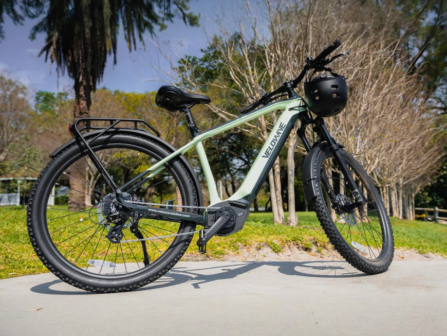Electric bike with a helmet on a paved path in a park. Valowave Swift M Mid-Drive Electric Bike