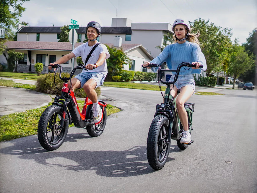 Two people riding electric bikes on a suburban street. Valowave Pony Compact Step-Thru Electric Bike