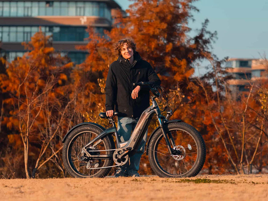 Person standing next to an electric bike with autumn trees and buildings in the background. Valowave Grace 2.0 Step-Thru Electric Bike