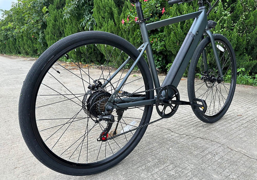Gray bicycle on a paved road with greenery in the background. Freego E7 Electric Bicycle For City Commuting
