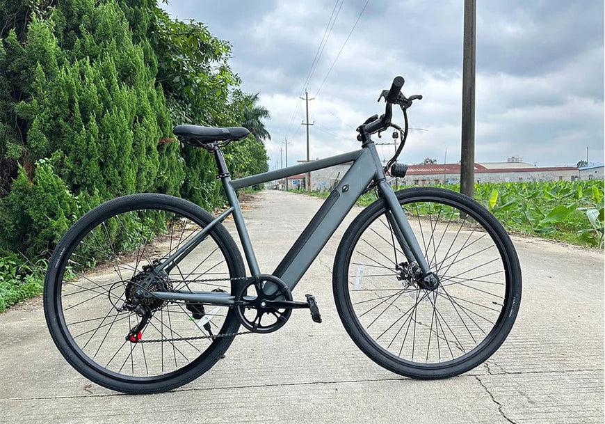 Gray electric bicycle on a paved road with greenery in the background. Freego E7 Electric Bicycle For City Commuting
