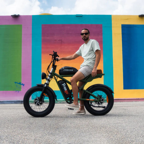 Man sitting on a green electric bike in front of a colorful mural. Freego Flash F3 Pro Dual Motor and Battery eBike