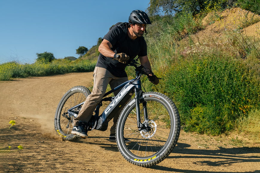 Man riding a mountain bike on a dirt trail with greenery in the background. CYKE Falcon S Full Suspension Ebike