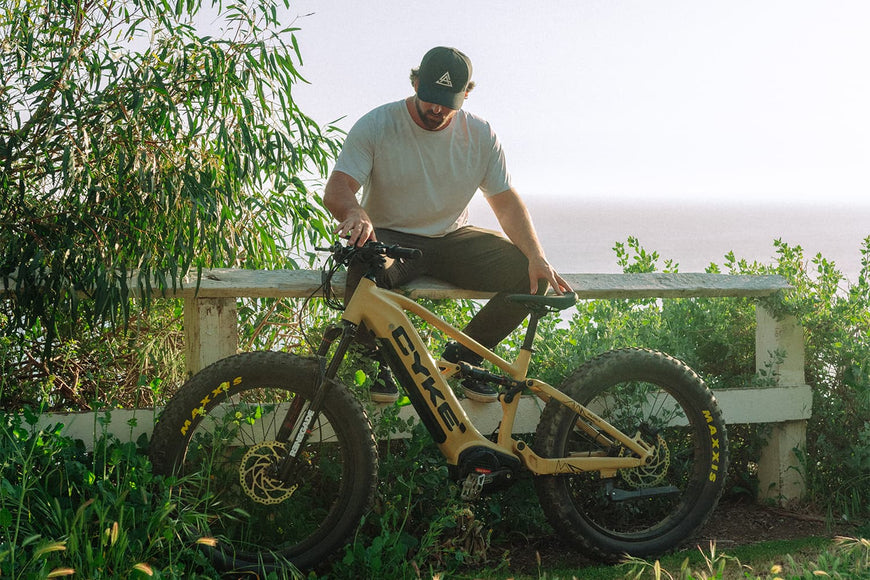 Man sitting on a yellow electric bike with a scenic background. CYKE Falcon X Full Suspension EBike