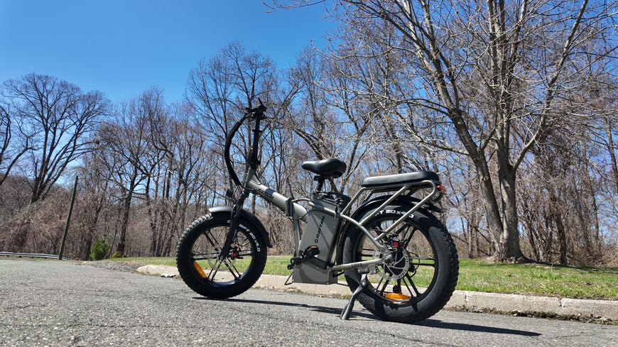 Folding electric bike on a paved road with leafless trees in the background. Rattan LM Ultra Folding ebike