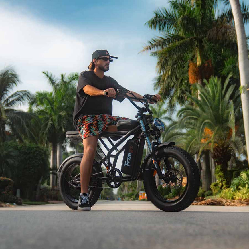 Man riding an electric bike in a tropical setting with palm trees. Freego Shotgun Prime F2 Pro Electric Cargo Bike