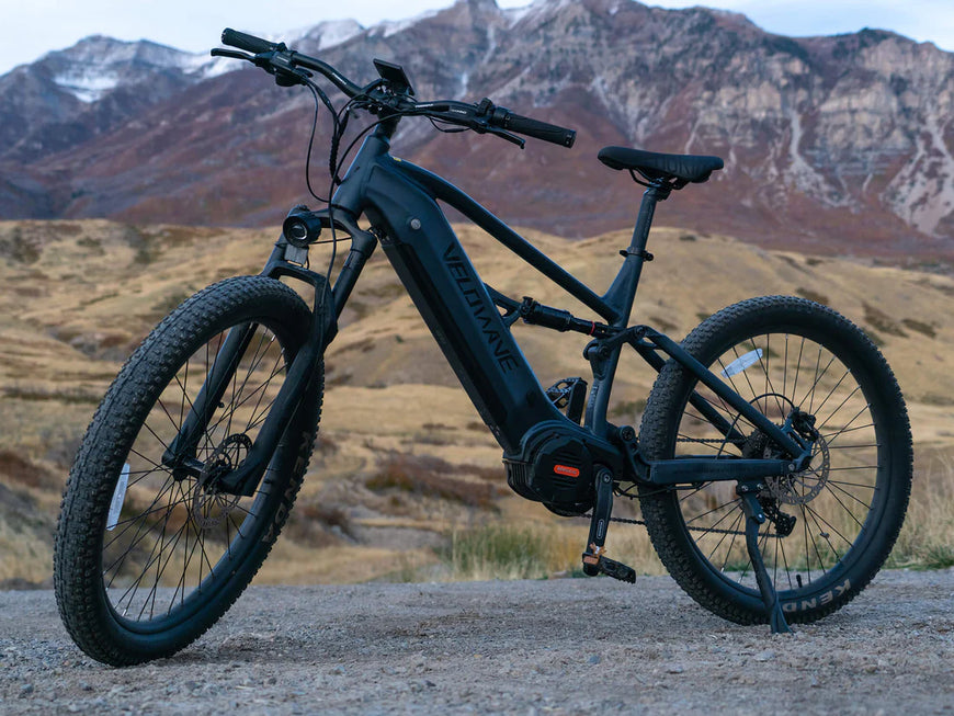 Black electric bike on a mountain trail with mountains in the background. Valowave Forest XM MTB
