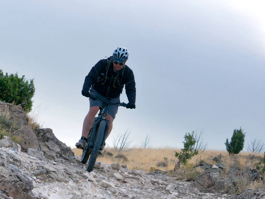 Person mountain biking on a rocky trail with a clear sky. Valowave Forest XM MTB