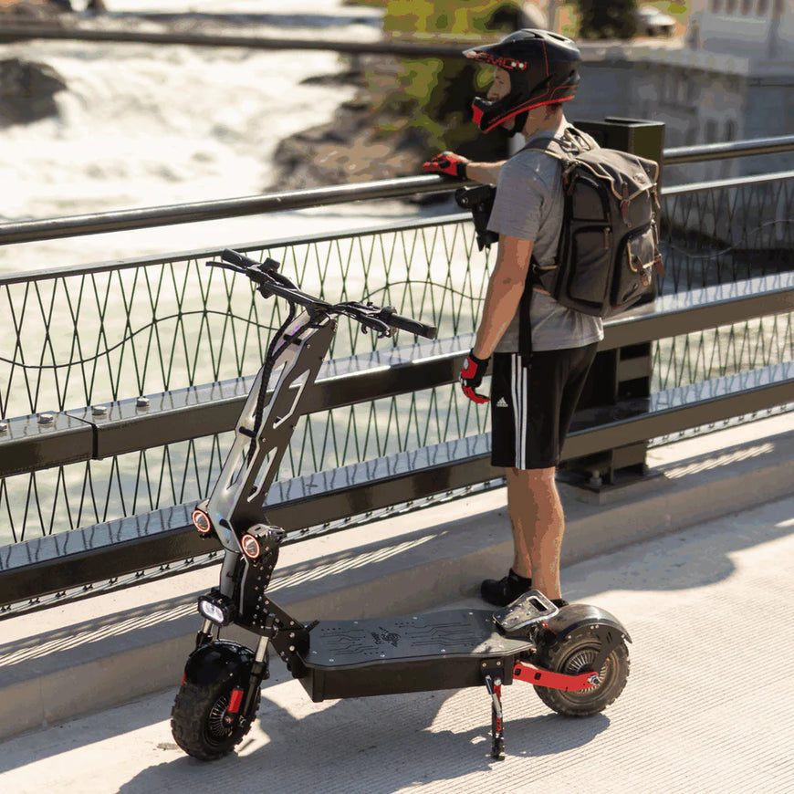 Person with a backpack standing next to a folded electric scooter on a bridge. Freego D11 Landtiger Electric Scooter Foldable Dual Motor 4000W