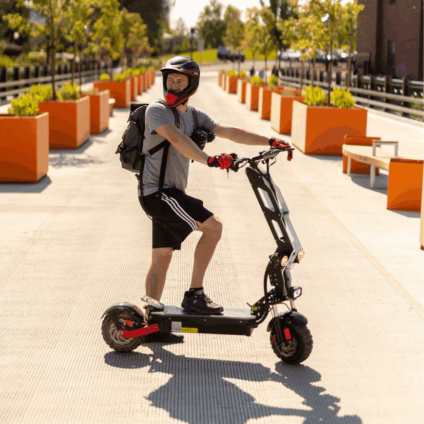 Person riding an electric scooter on a sidewalk with plants and buildings in the background. Freego D11 Landtiger Electric Scooter Foldable Dual Motor 4000W
