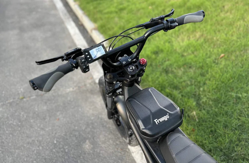Close-up of an electric bike handlebar with a Fragni brand logo on a grassy area. Freego Shotgun F2 Pro Max Prime Fat Tire E-Bike