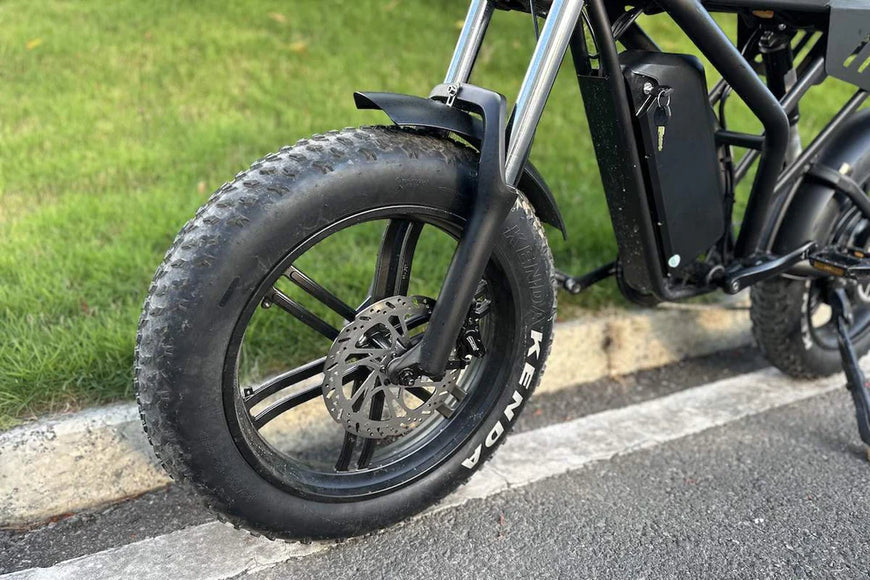 Close-up of a black electric bike tire on a road with grass in the background. Freego Shotgun F2 Pro Max Prime Fat Tire E-Bike