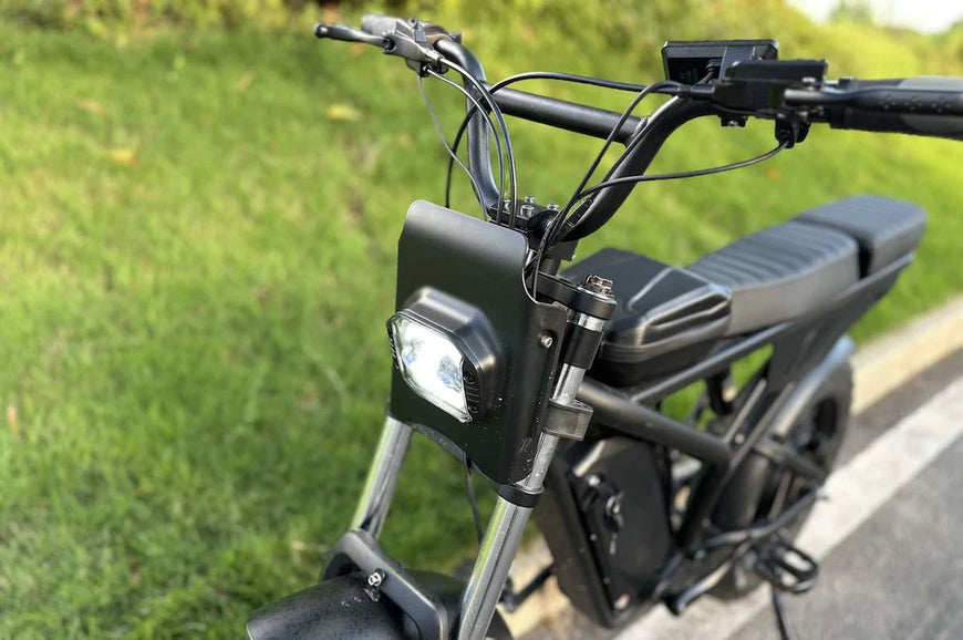 Close-up of a black electric bike with a headlight on a grassy background. Freego Shotgun F2 Pro Max Prime Fat Tire E-Bike