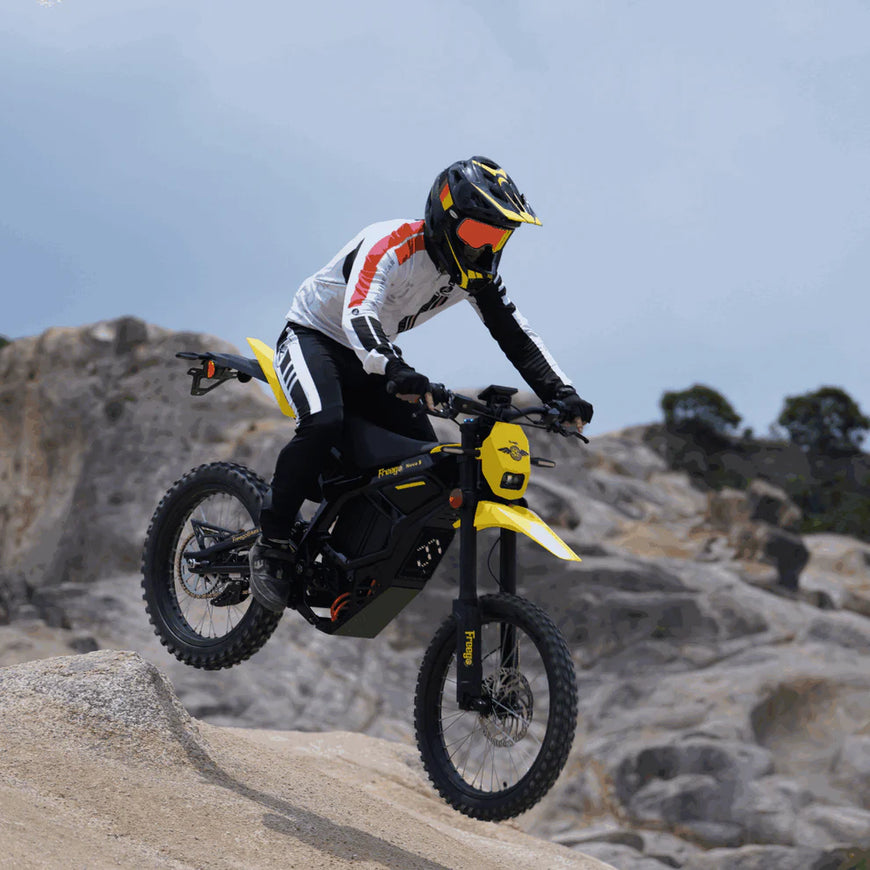 Person riding a yellow electric bike on rocky terrain with a helmet and protective gear. Freego Nova 5 Mid-Drive Off-Road Electric Dirt Bike