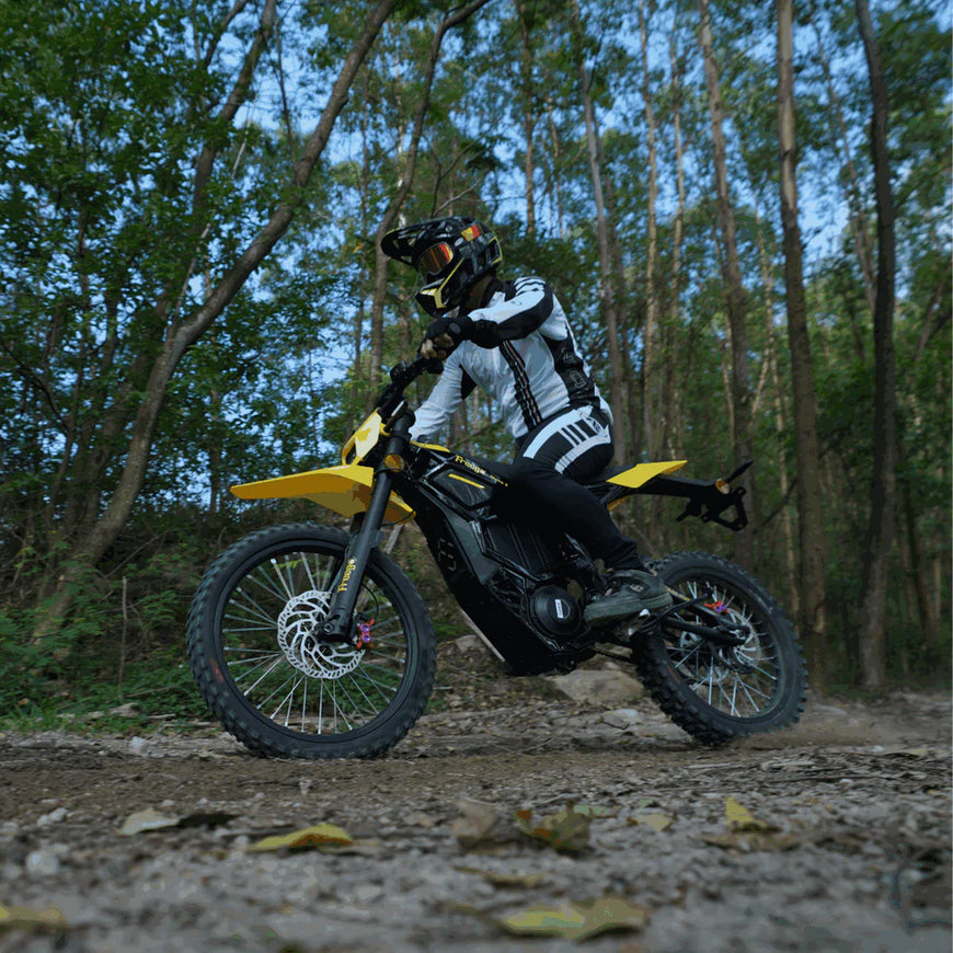 Person riding a yellow and black dirt bike on a trail in a forest. Freego Nova 5 Mid-Drive Off-Road Electric Dirt Bike