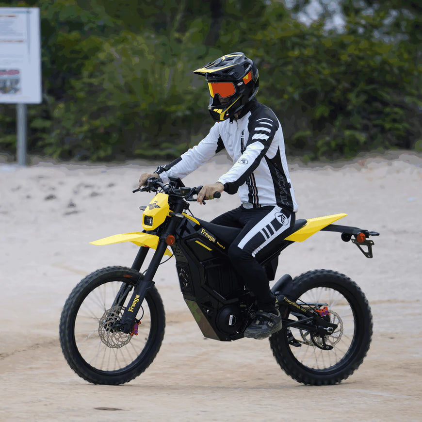 Person riding a yellow and black electric bike on a sandy surface with greenery in the background.Freego Nova 5 Mid-Drive Off-Road Electric Dirt Bike