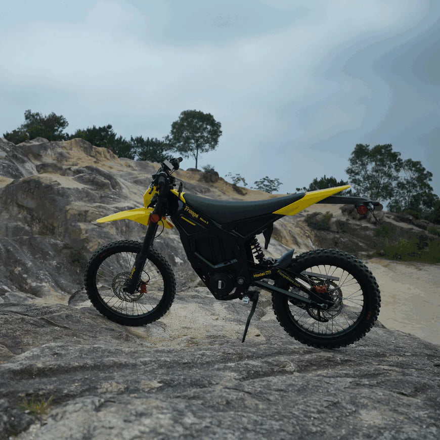 Yellow and black off-road motorcycle on a rocky terrain with trees in the background. Freego Nova 5 Mid-Drive Off-Road Electric Dirt Bike