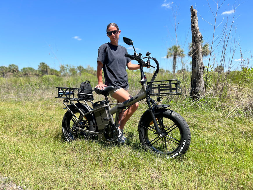Person sitting on an electric bike in a grassy field with trees in the background. Rattan LM Ultra Folding ebike