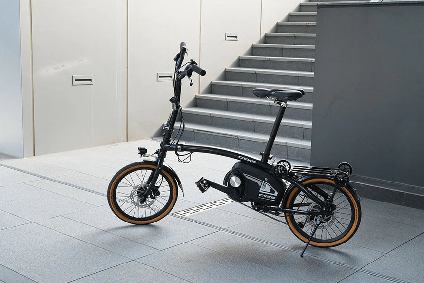 Foldable electric bike in a modern indoor setting with stairs. CYKE Kingfisher Mid-Drive Folding eBike