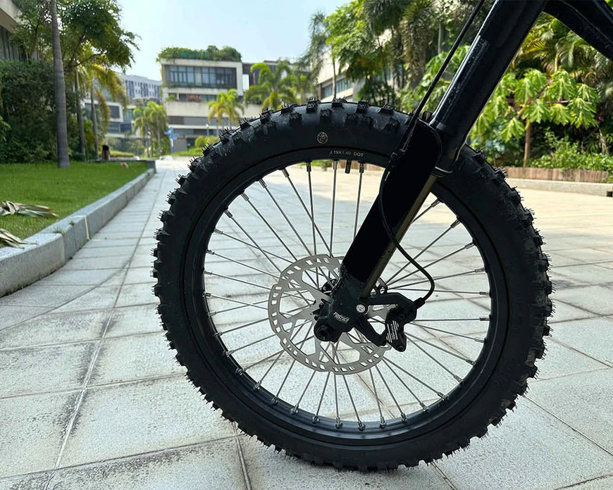 Close-up of a bicycle wheel on a paved path with greenery in the background. Natkie N1 All-Terrain Electric Motorcycle